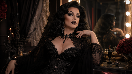Drag queen con look dark glam, peluca voluminosa, maquillaje dramático, vestuario negro brillante y accesorios de impacto en camerino teatral.